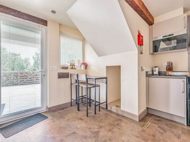A kitchen corner with a small table and two chairs under a slanted ceiling next to a door with blinds at Eden Mill Millers Beck in Kendal