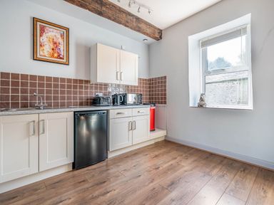 A kitchen with white cabinets a black mini fridge brown tiled backsplash and a window with a cat figurine on the sill at Eden Mill Millers Beck in Kendal