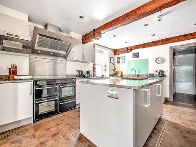 A kitchen with an island central countertop black oven wooden ceiling beams and a window at Eden Mill Millers Beck in Kendal