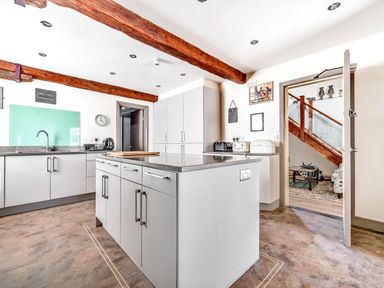 A kitchen with an island countertop wooden ceiling beams and a doorway leading to a room with stairs at Eden Mill Millers Beck Kendal