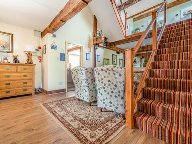 A seating area with two patterned armchairs on a rug next to a wooden staircase with striped carpet at Eden Mill Millers Beck in Kendal
