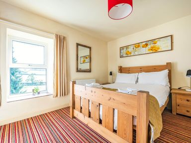 A bedroom with a wooden bed frame white bedding striped carpet and a window at Eden Mill Millers Beck in Kendal