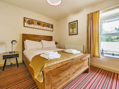 A bedroom with a wooden bed frame bedside table lamp striped carpet and window with curtains at Eden Mill Millers Beck in Kendal