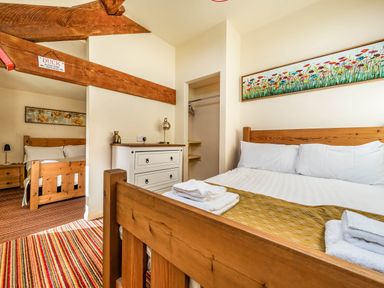 A bedroom with wooden beds white linens a white dresser and floral artwork at Eden Mill Millers Beck in Kendal