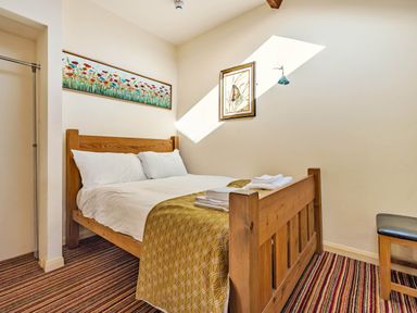 A bedroom with a wooden bed with white bedding and folded towels on a striped carpet at Eden Mill Millers Beck in Kendal