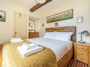 A bedroom with a wooden bed and nightstand a lamp folded towels on the bed and a chest of drawers at Eden Mill Millers Beck in Kendal