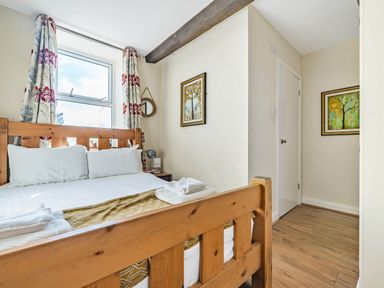 A bedroom with a wooden bed frame white bedding and folded towels near a window with floral curtains and framed pictures on the walls at Eden Mill Millers Beck in Kendal