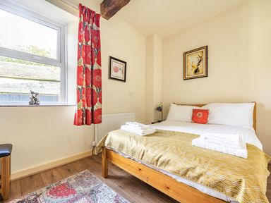 A bedroom with a wooden bed white bedding and yellow cover next to a window with red floral curtains at Eden Mill Millers Beck in Kendal