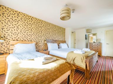 A bedroom with two beds bedside tables patterned wallpaper and a chest of drawers at Eden Mill Millers Beck in Kendal