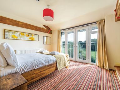 A bedroom with a wooden bed a striped carpet and glass doors overlooking greenery at Eden Mill Millers Beck in Kendal