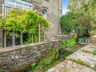 A stone building with a wooden trellis covered in plants beside a flowing water channel at Eden Mill Millers Beck in Kendal