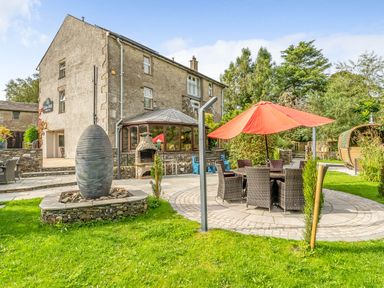 A stone building with outdoor seating and an umbrella near a garden at Eden Mill Millers Beck in Kendal