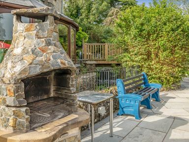 An outdoor stone barbecue grill with a metal small table and a blue bench on a patio at Eden Mill Millers Beck in Kendal