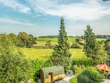 A garden with a wooden cabin a patio with table and chairs and a red umbrella overlooking fields at Eden Mill Millers Beck in Kendal