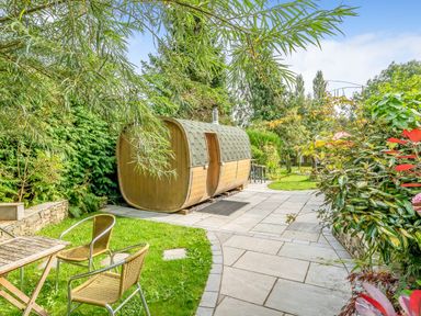 A garden with a wooden barrel sauna on a paved area metal chairs and table on grass at Eden Mill Millers Beck in Kendal