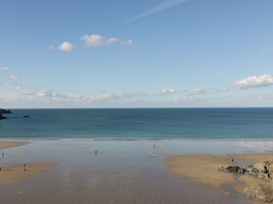 A wide beach with a few people walking near the water with blue ocean and sky at Buena Vista in Newquay