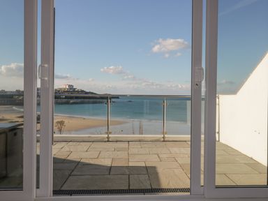 A balcony with glass railing overlooking a beach and sea at Buena Vista in Newquay
