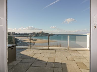 A balcony with stone tiles and a glass railing overlooking a sandy beach and ocean at Buena Vista in Newquay
