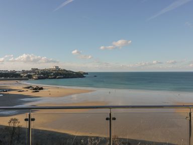 A beach with sand and water visible beyond a glass railing at Buena Vista in Newquay