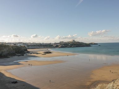 A wide sandy beach with a few people walking near the shore and a town with buildings in the background at Buena Vista in Newquay