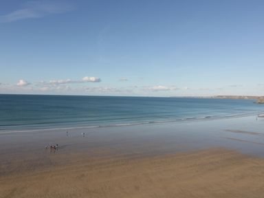 A beach with people walking near the water and a distant coastline at Buena Vista in Newquay