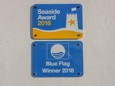 Two blue and yellow award plaques on a white wall displaying seaside award and blue flag winner 2018