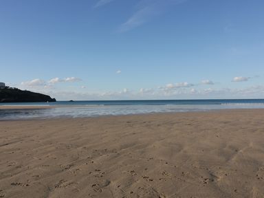 A sandy beach with footprints leading to the sea and a distant headland under a clear blue sky at Buena Vista in Newquay