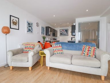 A living room with two sofas a yellow side table and a dining area with orange chairs at Buena Vista in Newquay