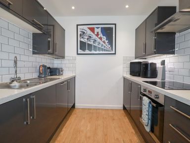 A kitchen with gray cabinets white tiled backsplash wooden floor and appliances at Buena Vista in Newquay