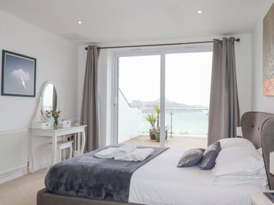 A bedroom with a bed, dressing table, and sliding glass doors leading to a balcony at Buena Vista in Newquay