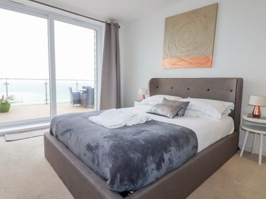 A bedroom with a bed a gray blanket and sliding glass doors leading to a balcony at Buena Vista in Newquay