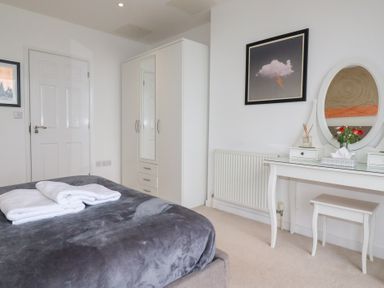 A bedroom with a bed, white wardrobe, white dressing table with mirror and stool at Buena Vista in Newquay