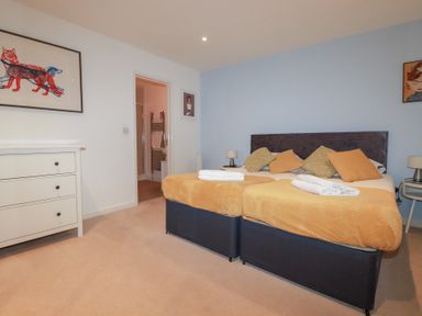 A bedroom with a double bed with orange covers and pillows a white dresser and a door leading to a bathroom at Buena Vista in Newquay