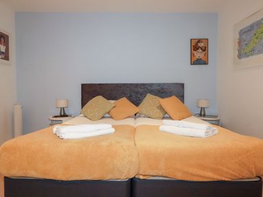 A bedroom with two single beds pushed together orange bed covers four pillows and two bedside tables with lamps at Buena Vista in Newquay