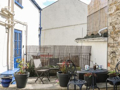 An outdoor patio with metal chairs a table with a coffee press and mugs and potted plants at The Compass in Swanage