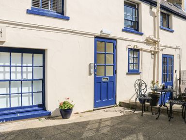 A courtyard with blue doors and windows a table with two chairs and potted plants at The Compass in Swanage