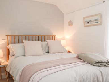 A bedroom with a wooden bed frame pillows blankets nightstands with lamps a clock and a framed picture at The Compass in Swanage