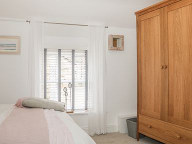 A bedroom with a wooden wardrobe a window with blinds and curtains and a bed with folded blankets at The Compass in Swanage
