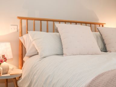 A bed with striped bedding and large pillows next to a white side table with a lamp and flowers at The Compass in Swanage