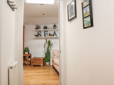 A hallway leading to a room with wooden floor a wooden table a couch plants and wall shelves with decorative items at The Compass in Swanage
