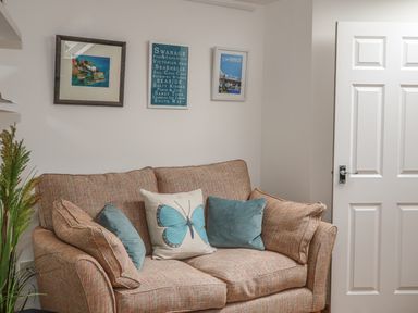 A sofa with cushions and framed pictures on a wall next to a white door at The Compass in Swanage