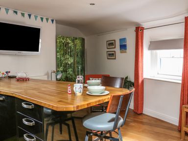 A kitchen area with a wooden countertop and chairs near a window with red curtains at The Compass in Swanage