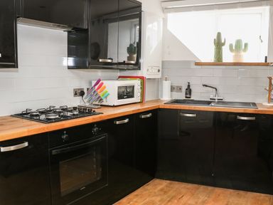 A kitchen with black cabinets wooden countertop gas stove oven microwave sink and window with cactus pots at The Compass in Swanage