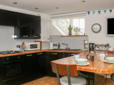 A kitchen with black cabinets wooden countertops a stove microwave sink mugs and bowls on a table at The Compass in Swanage