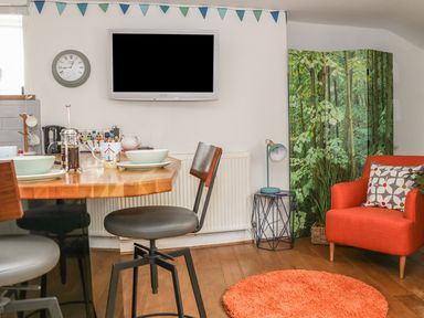 A dining area with a wooden table set with bowls and mugs next to an orange armchair and a forest-themed folding screen at The Compass in Swanage
