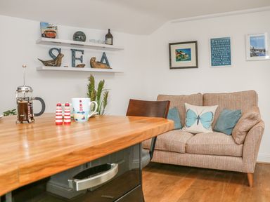 A seating area with a couch and wall art beside a wooden table with a coffee press and mug at The Compass in Swanage