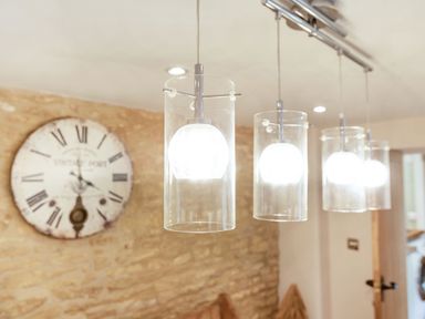 A row of hanging pendant lights with glass covers and a wall clock with Roman numerals on a stone wall at Puffitts Cottage in Bourton-on-the-Water