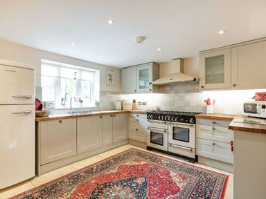 A kitchen with white cabinets wooden countertops a stove a refrigerator and a patterned rug on the floor at Puffitts Cottage in Bourton-on-the-Water