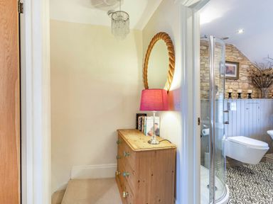 A small hallway with a wooden dresser and lamp next to a bathroom with a shower and toilet at Puffitts Cottage in Bourton-on-the-Water