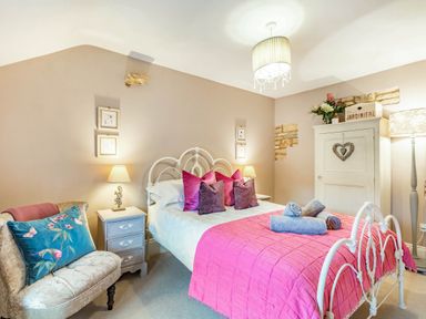 A bedroom with a metal bed frame pink bedspread and folded towels on the bed at Puffitts Cottage in Bourton-on-the-Water